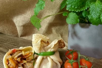 Powiększ obraz: fot. facebook Look-Cook Catering, www.facebook.com/LOOKCOOKCatering/?ref=page_internal. Na zdjęciu mały zawinięty naleśnik, obok niego przekrojony naleśnik z pokrojoną marchewką, kaszą i innymi dodatkami, na stole leżą też pomidorki koktajlowe, po prawej stronie doniczka z miętą