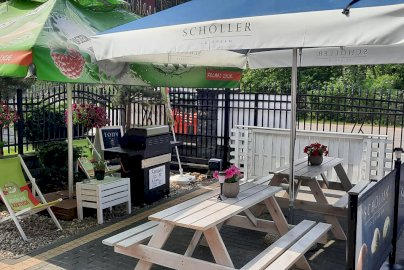 Powiększ obraz: fot. facebook Azyl Cafe, www.facebook.com/azylcafedosin/. Na zdjęciu parasole, pod nimi znajdują się stoliki z ławkami, leżaki,  na drewnianym stoliku  doniczka z kwiatem