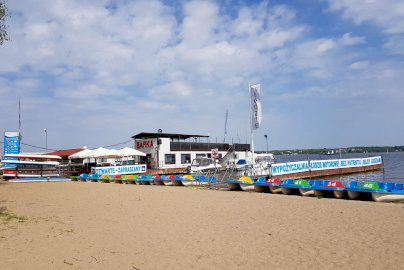 Powiększ obraz: fot. www.water-club.pl/restauracja/restauracja-barka. Na zdjęciu plaża, restauracja BARKA, napis na banerze: wypożyczalnia, łodzie motorowe, bez patentu, rejsy łodziami, jezioro zegrzyńskie