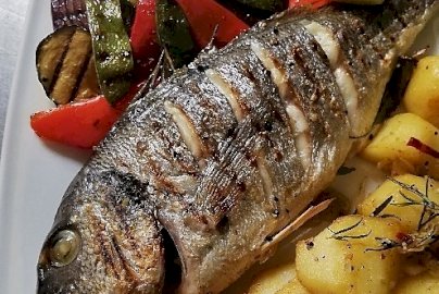 Powiększ obraz: fot. firstwarsaw.pl/restauracja-menu/. Na zdjęciu ryba smażona w całości, pieczone ziemniaki w kawałkach, warzywa na talerzu