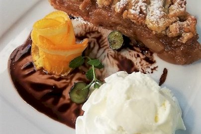 Powiększ obraz: fot. firstwarsaw.pl/restauracja-menu/. Na zdjęciu szarlotka - ciasto, bita śmietana, polewa czekoladowa na talerzu