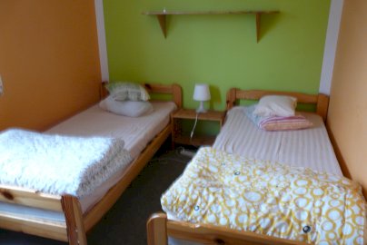 Powiększ obraz: fot. www.stajniaklucz.pl. Na zdjęciu dwa pojedyncze łóżka, nad łóżkiem półka, lampka na szafce