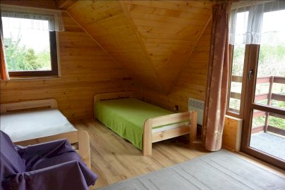 Powiększ obraz: fot. wwww.swiecienica.wixsite.com/rybaczowka. Na zdjęciu pokój z 2 pojedynczymi łóżkami, fotel, drzwi balkonowe, okno