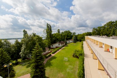 Powiększ obraz: fot. www.geovita.pl/jadwisin/. Na zdjęciu hotel Geovita w Jadwisinie - tarasy, domki, wokół zieleń, drzewa, po lewej stronie rzeka Narew