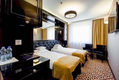 Powiększ obraz: fot. www.hotel500.com.pl/zegrze. Na zdjęciu pokój hotelowy, dwa pojedyncze łóżka z poduszkami i pościelą, dwa fotele przy oknie, na ścianie telewizor, butelki z wodą, pilot od telewizora na szafce