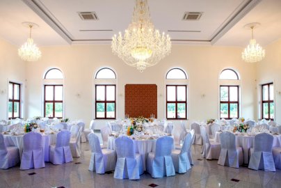 Powiększ obraz: fot. www.rozany-dwor.pl, na zdjęciu sala weselna dla gości z stolikami i krzesełkami, zapalone żyrandole nad stolikami, z 6 okien widok na otoczenie