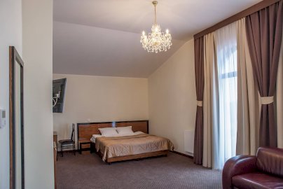 Powiększ obraz: fot. www.rozany-dwor.pl. Na zdjęciu pokój hotelowy z łożem, telewizor po lewej stronie, stolik z krzesłem, brązowa kanapa