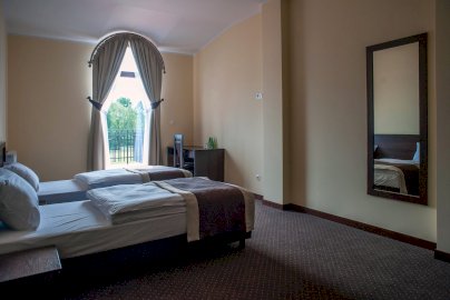 Powiększ obraz: fot. www.rozany-dwor.pl. Na zdjęciu pokój hotelowy z dwoma pojedynczymi łóżkami, prześcieradłami, lustrem