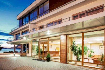 Powiększ obraz: fot. www.marinadiana.pl. Na zdjęciu Hotel Marina Diana w Białobrzegach, wewnątrz oświetlona recepcja z kontuarem, miejscem do siedzenia na kanapie, stojącymi kwiatami wewnątrz hotelu