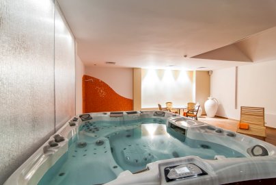 Powiększ obraz: Fot. www.windsorhotel.pl. Na zdjęciu jacuzzi z dyszami, leżak, w oddali stolik z krzesełkami