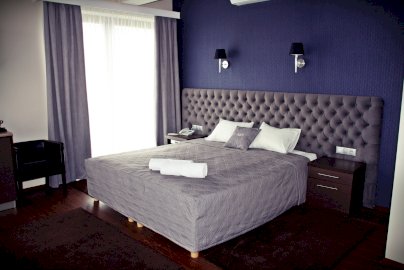 Powiększ obraz: fot. www.villamalibu.pl,  na zdjęciu pokój hotelowy z obszernym łóżkiem, gdzie leżą poduszki, ręczniki hotelowe, po obydwu stronach szafki