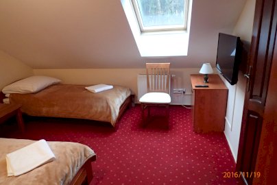 Powiększ obraz: fot. www.zajazdross.pl.  Na zdjęciu pokój hotelowy zajazdu Ross w Nieporęcie, dwa pojedyncze łóżka, TV, nad krzesłem okno dachowe