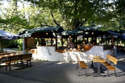 Powiększ obraz: fot. windsorhotel.pl. Na zdjęciu kucharz przygotowuje posiłki w altanie grillowej, na zewnątrz altany stoliki z ławkami do siedzenia, po prawej stronie artykuły spożywcze, dania na stole