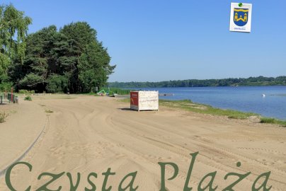 Powiększ obraz: fot. UG Wieliszew, www.wieliszew.pl. Na zdjęciu plaża w Wieliszewie, bliżej brzegu rzeki drewniana skrzynia, po prawej stronie rzeka Narew, w tle z tyłu drzewa, na dole zdjęcia napis Czysta Plaża,  w prawym górnym rogu herb Urzędu Gminy Wieliszew