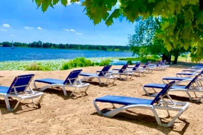 Powiększ obraz: fot. www.hotel500.com.pl/zegrze. Na zdjęciu leżaki w kolorze niebieskim rozstawione na plaży Hotelu500 w Zegrzu, z tyłu w tle widok na Jezioro Zegrzyńskie, na górze korona drzewa liściastego
