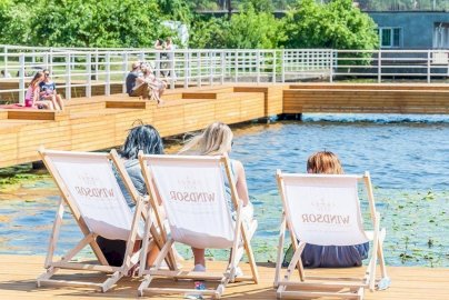 Powiększ obraz: fot. windsorhotel.pl. Na zdjęciu kobiety siedzą na leżakach, jedna z nich siedzi na pomoście, z tyłu drewniany pomost, budynek mieszkalny, drzewa