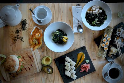Powiększ obraz: fot. Hokano Sushi, www.facebook.com/NoweHokanoSushi. Na zdjęciu sushi, dzbanek, filiżanki z  talerzykami, krewetki na talerzyku, awokado, burger na desce