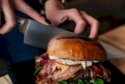 Powiększ obraz: fot. www.trustburger.pl/galeria. Na zdjęciu osoba  krojąca burgera