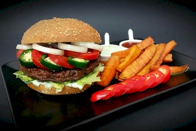 Powiększ obraz: fot. www.beef-burger.pl/. Na zdjęciu burger z mięsem, cebulą, pomidorami, papryczką, sałatą, obok frytki, sosy