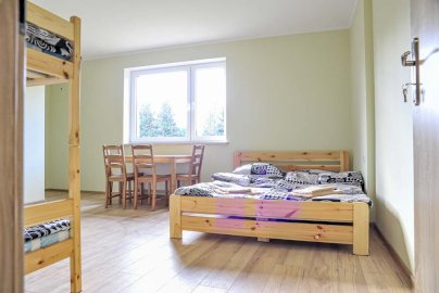 Powiększ obraz: fot. www.farmaserock.pl/baza-noclegowa/. Na zdjęciu szerokie łóżko do spania, obok mniejsze piętrowe łóżko, stolik z krzesłami przy oknie