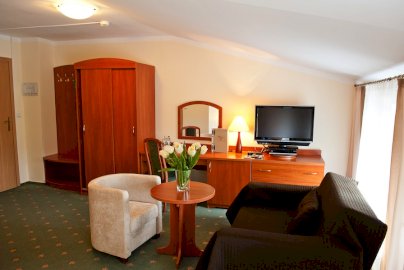 Powiększ obraz: fot. www.zlotylin.pl. Na zdjęciu pokój hotelowy, na stoliku wazon z kwiatami, fotele, na szafce stoi telewizor, biurko z krzesłem, lustro na ścianie, szafka na garderobę, wieszaki, fragment drzwi wejściowych do pokoju