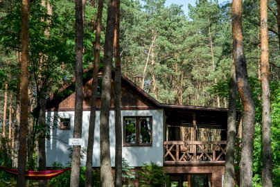 Powiększ obraz: fot. https://www.airbnb.pl/rooms/40772400/photos?source_impression_id=p3_16463050fot. 43_gdiL3KEzmTofvsN1&modal=PHOTO_TOUR_SCROLLABLE. Na zdjęciu domek w otoczeniu drzew Masuria Warsaw, kolorowy hamak wiszący na drzewach