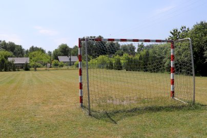 Powiększ obraz: fot. https://www.osirjablonna.pl/baza-sportowa/boisko-w-suchocinie#gallery-6. Na zdjęciu boisko o naturalnej nawierzchni do gry w piłkę nożną, z tyłu domy mieszkalne