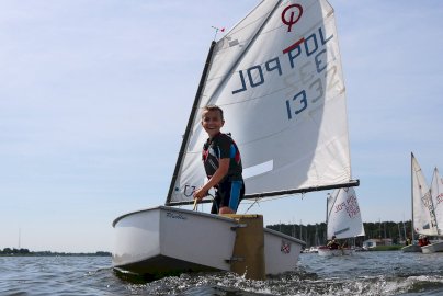 Powiększ obraz: fot. https://ykpwarszawa.pl/port-pilawa/. Na zdjęciu uśmiechnięty chłopiec pływa na żaglach na wodzie