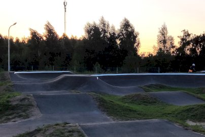 Powiększ obraz: Na zdjęciu panorama pumptracku w Skubiance z falistymi przeszkodami, na tle zachodzącego słońca