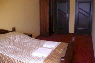 Powiększ obraz: fot. https://salamario.pl/galeria/. Na zdjęciu pokój  hotelowy w hotelu Mario, łóżko do spania, wysoka szafa na ubrania, drzwi wejściowe do pokoju