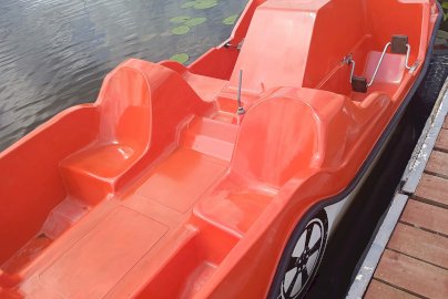 Powiększ obraz: fot. Ośrodek Sportów Wodnych PORT AZS ZEGRZE. Na zdjęciu rowerki wodne w kształcie samochodu barwy czerwonej, z tyłu rowerki wodne o różnych kolorach stojące przy brzegu