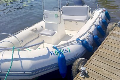 Powiększ obraz: fot. Ośrodek Sportów Wodnych PORT AZS ZEGRZE. Na zdjęciu łódź motorowodna. W środku łodzi siedziska, kierownica, wiszące czerwone koło ratunkowe z tyłu łodzi