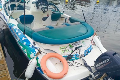 Powiększ obraz: fot. Ośrodek Sportów Wodnych PORT AZS ZEGRZE. Łódź motorowodna. W środku łodzi widać siedzenia, zadaszenie nad łodzią, koło ratunkowe przymocowane do łodzi, silnik Mercury. Z przodu kilka łodzi motorowych dryfujących na wodzie