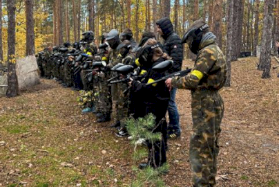 Powiększ obraz: Fot. EVENT EXTREME FORT ROBSON. Uczestnicy w maskach i odzieży ochronnej stoją w rzędzie w lesie i trzymają markery paintballowe podczas przygotowania do gry w paintballa