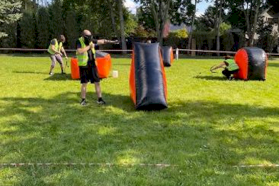 Powiększ obraz: Fot. EVENT EXTREME FORT ROBSON. Na zdjęciu kilka osób gra w paintball na trawiastej polanie, chowając się za nadmuchiwanymi przeszkodami i celując z markerów