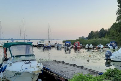 Powiększ obraz: fot. Klub Dolomit w Jadwisinie. Na zdjęciu przedstawiono niewielką przystań z łodziami zacumowanymi przy drewnianym pomoście