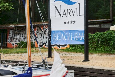 Powiększ obraz: Fot. Hotel Narvil. Zdjęcie przedstawia przystań Hotelu Narvil z łodziami i rowerami wodnymi przy Narvil Beach Bar zachęca do relaksu oraz aktywnego wypoczynku nad wodą